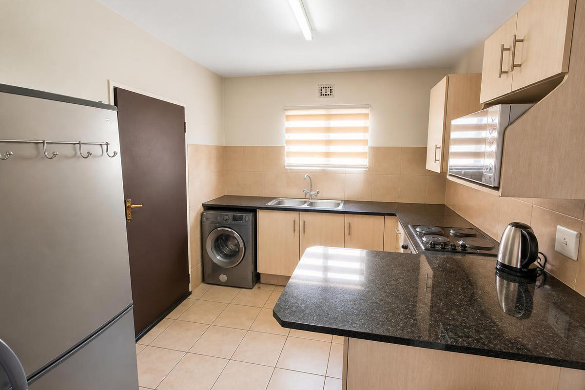 Functional kitchen featuring granite countertops, built-in cabinetry, integrated hob and oven, and tiled flooring with a dedicated space for laundry appliances.
