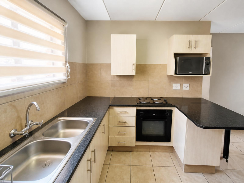 A clean, functional kitchen featuring granite countertops, built-in oven and hob, double sink, and light-toned cabinetry with ample storage space.