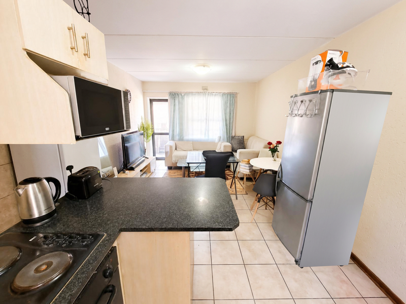 Open-plan kitchen and living area featuring tiled flooring, built-in cabinetry, and integrated kitchen appliances, leading to a bright lounge space.