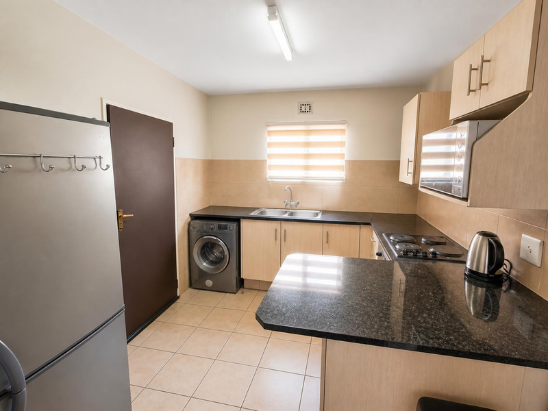 Functional kitchen featuring granite countertops, built-in cabinetry, integrated hob and oven, and tiled flooring with a dedicated space for laundry appliances.