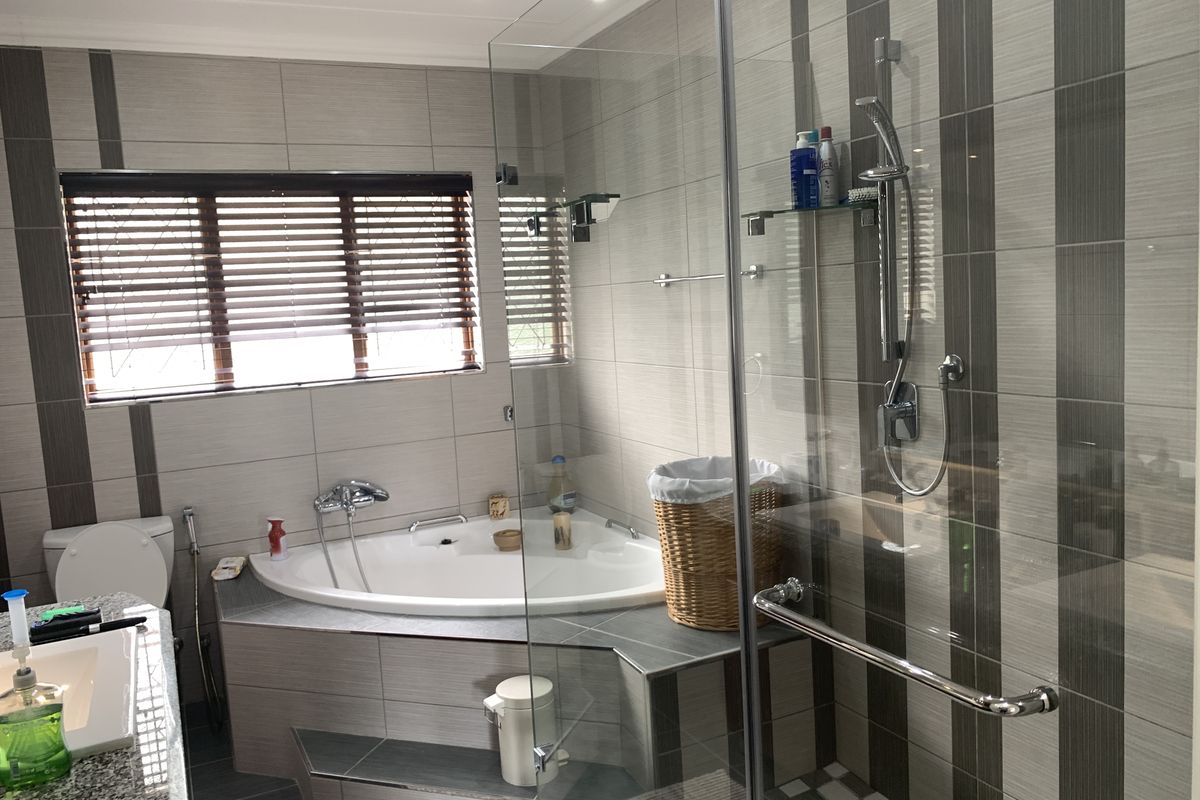 Modern bathroom featuring a corner bathtub, separate glass-enclosed shower, granite-topped vanity, and contemporary striped wall tiling.