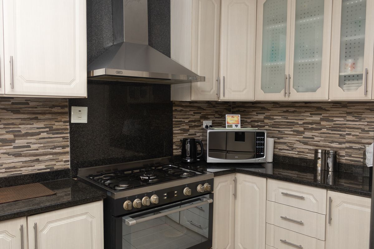 A well-maintained kitchen featuring granite countertops, stone tile backsplash, built-in gas stove with extractor fan, and ample cabinetry with glass-fronted display units.