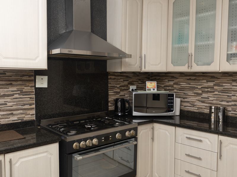 A well-maintained kitchen featuring granite countertops, stone tile backsplash, built-in gas stove with extractor fan, and ample cabinetry with glass-fronted display units.