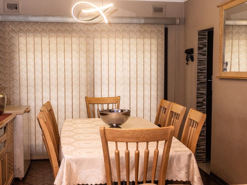 A dining room featuring tiled flooring, vertical blinds, and a modern pendant light fixture, providing a functional space for family meals.