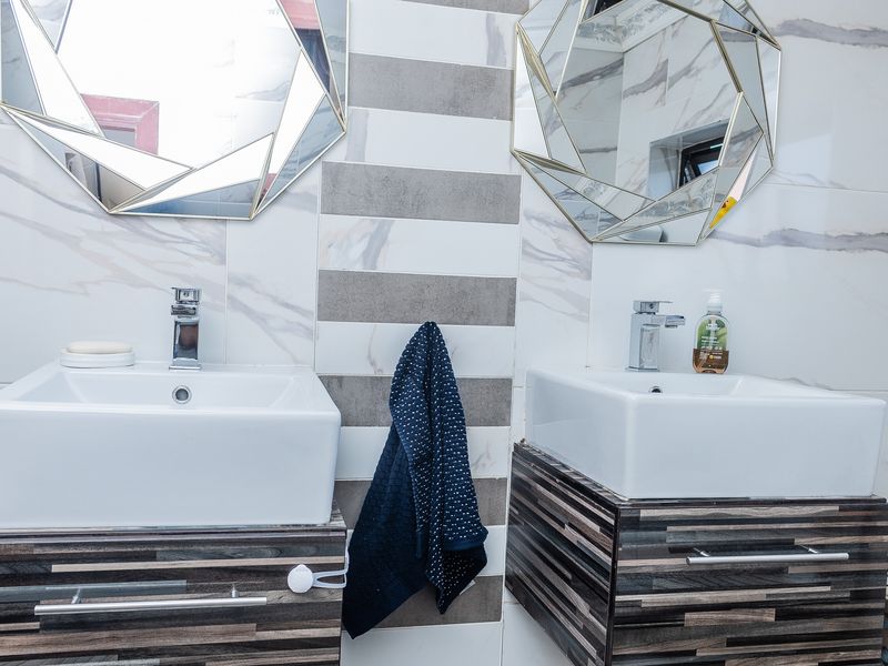 A modern bathroom featuring a double vanity with vessel sinks, chrome faucets, and decorative wall-mounted mirrors against a tiled feature wall.