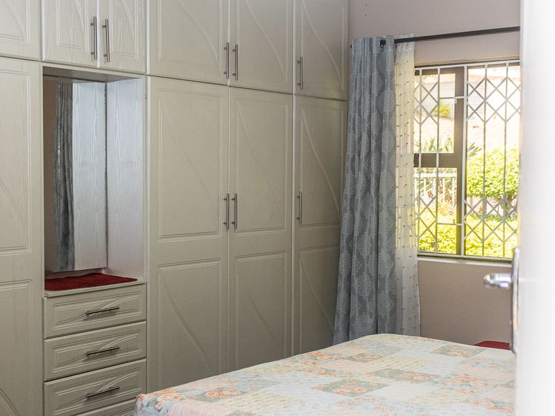 A well-maintained bedroom featuring extensive floor-to-ceiling built-in cupboards with an integrated vanity area and secure window fittings.
