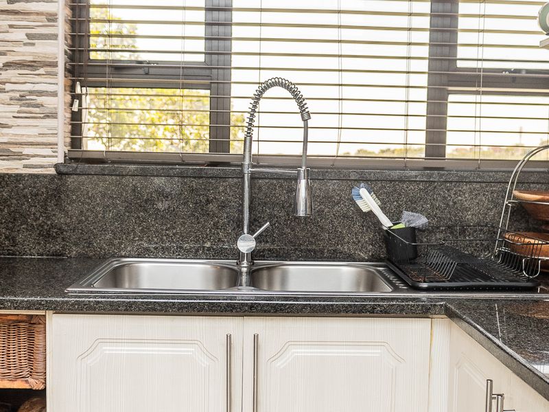 A well-maintained kitchen area featuring a double bowl stainless steel sink, granite countertops, and modern gooseneck faucet set against a stone-tiled feature wall.