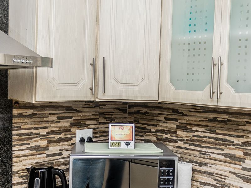 A well-maintained kitchen corner featuring granite countertops, stone tile backsplash, and built-in cabinetry with integrated microwave and extractor fan.