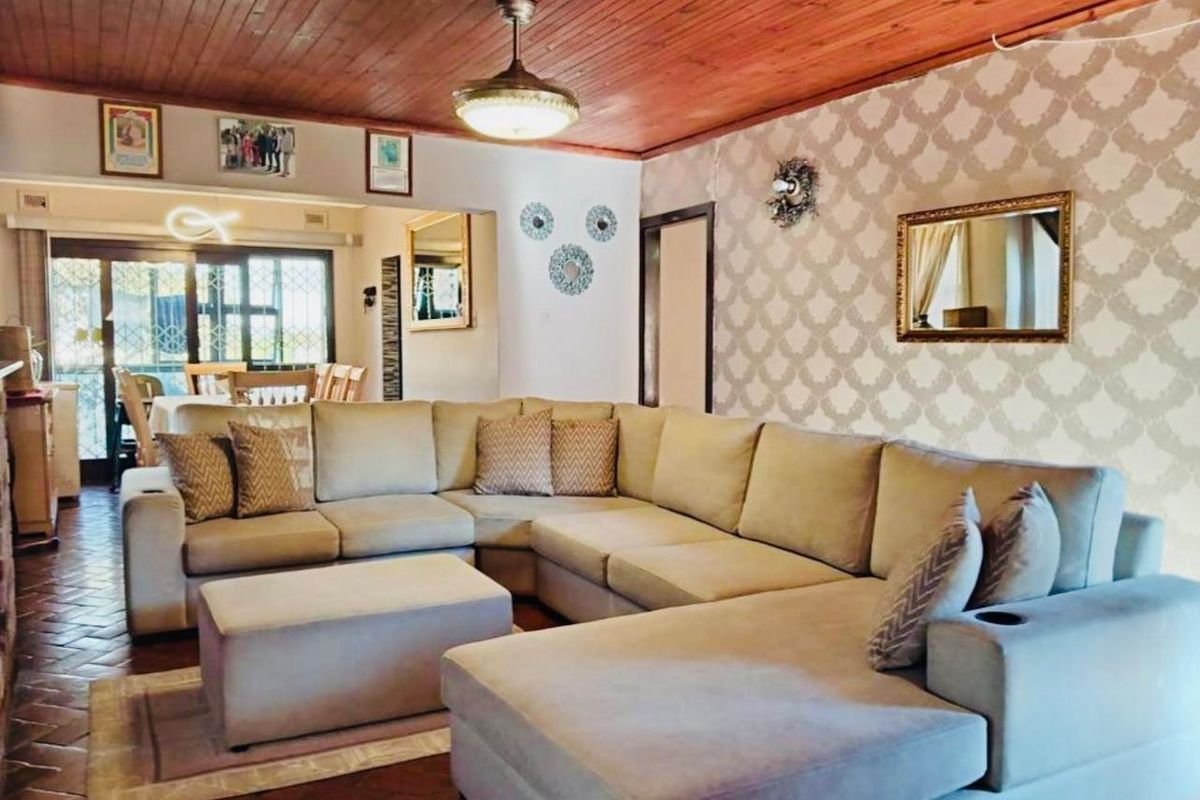 Spacious living room featuring a timber ceiling, ceiling fan, patterned wallpaper, and terracotta floor tiles, with an adjacent dining area visible through the sliding door.