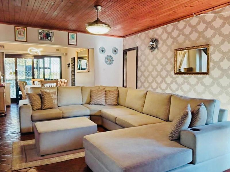 Spacious living room featuring a timber ceiling, ceiling fan, patterned wallpaper, and terracotta floor tiles, with an adjacent dining area visible through the sliding door.