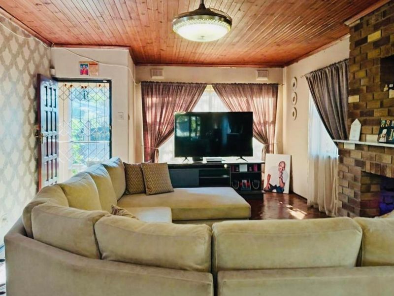 A living room featuring a brick fireplace, timber ceiling, and hardwood flooring, providing a cozy, traditional atmosphere with potential for modern updates.