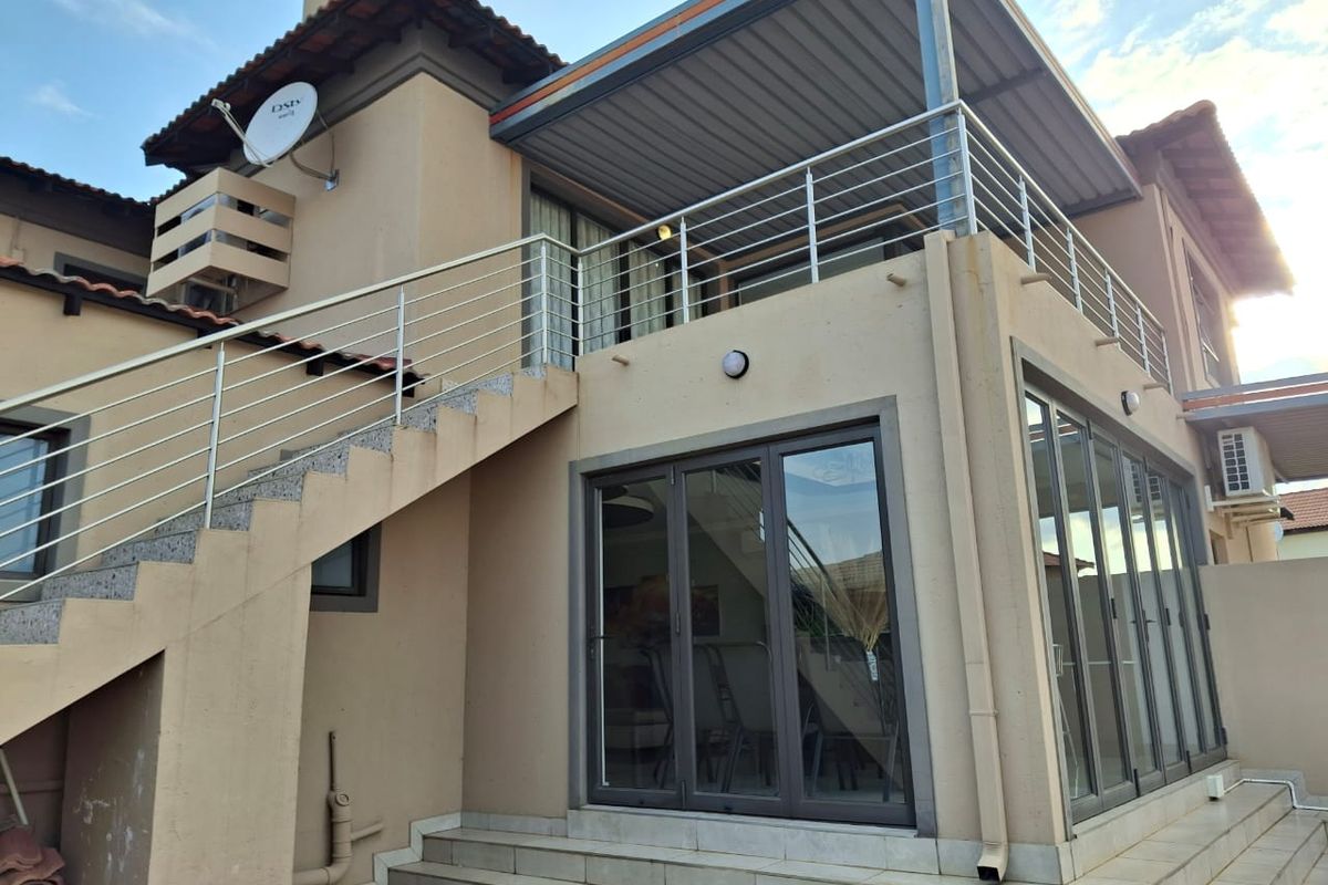 Rear exterior view of a multi-level home featuring a covered balcony, stainless steel balustrades, and modern aluminium folding doors leading to a tiled patio area.