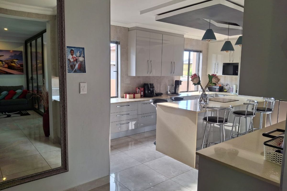 Modern kitchen featuring high-gloss cabinetry, stone countertops, a central island with breakfast bar seating, and stylish pendant lighting under a recessed ceiling.