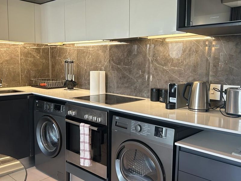 Modern kitchen featuring sleek cabinetry, stone countertops, marble-look splashback, integrated appliances, and under-cabinet lighting for a contemporary and functional workspace.
