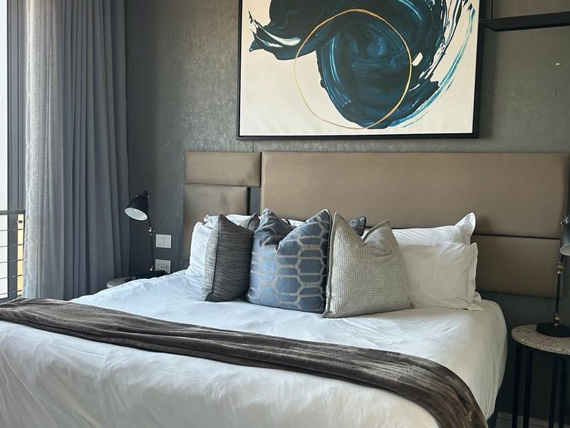 A well-appointed bedroom featuring a large upholstered headboard, modern finishes, and direct access to a private balcony through sliding glass doors.
