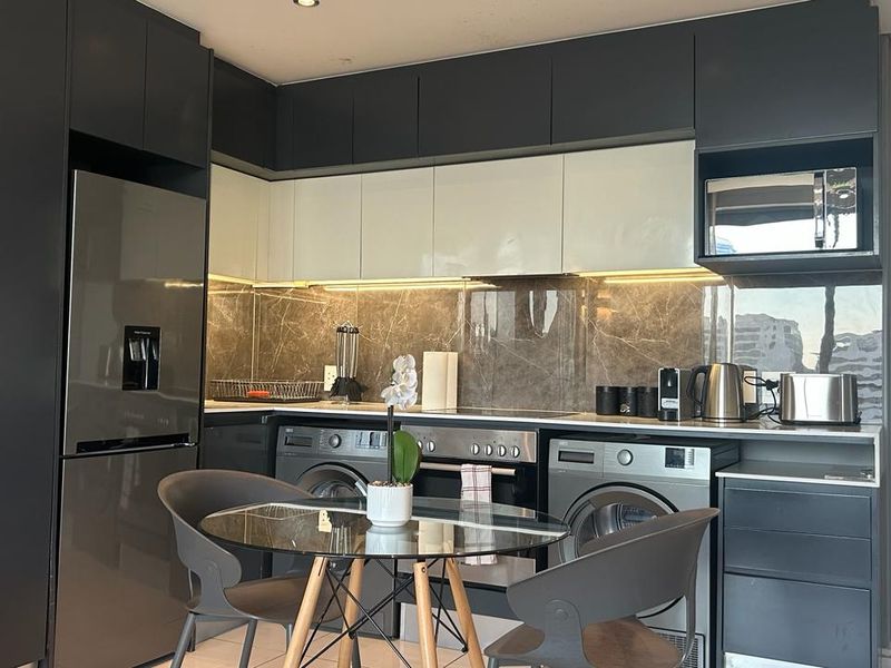 Modern kitchen featuring sleek dark and light cabinetry, stone splashback, integrated appliances, and recessed lighting in a compact, functional layout.