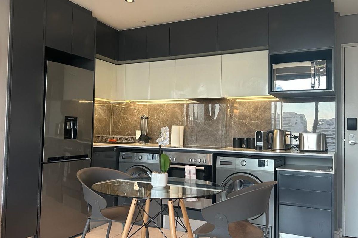 Modern kitchen featuring sleek dark and light cabinetry, stone splashback, integrated appliances, and recessed lighting in a compact, functional layout.
