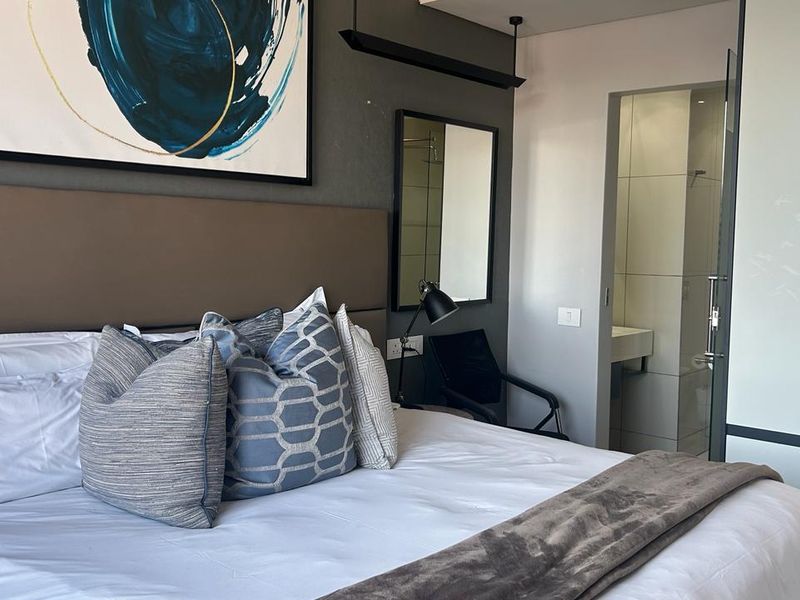 Modern bedroom featuring a built-in headboard, integrated wardrobe, and direct access to an en-suite bathroom with contemporary finishes.