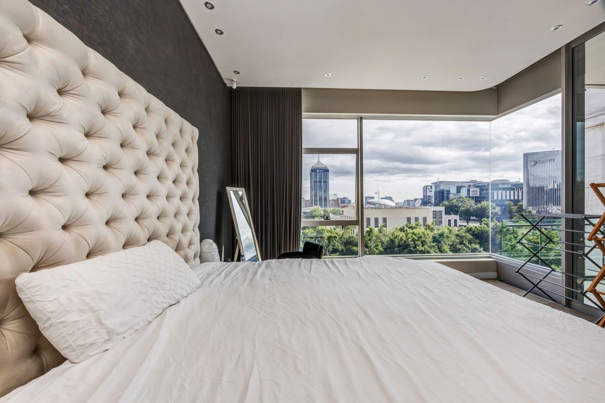 Modern bedroom featuring floor-to-ceiling windows with expansive city views, recessed lighting, and a sophisticated accent wall.