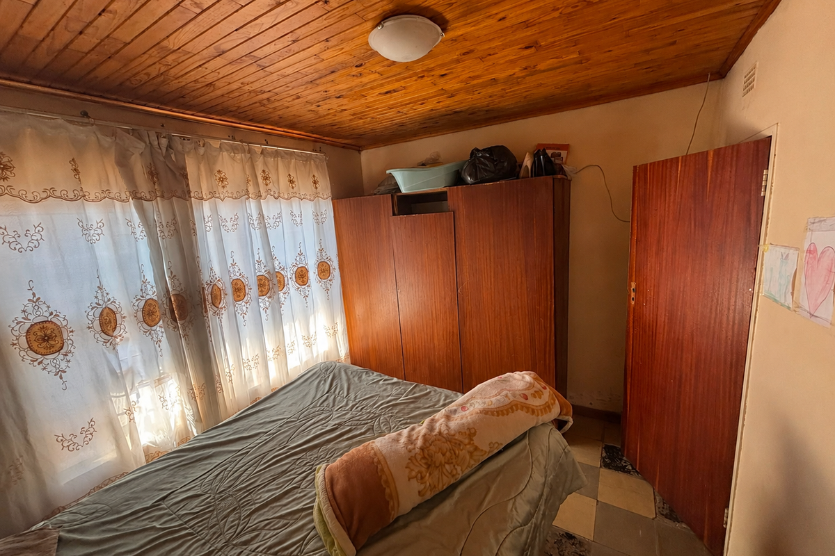 A bedroom featuring a timber tongue and groove ceiling, built-in wardrobe, and tiled flooring, requiring cosmetic updates to improve its overall condition.