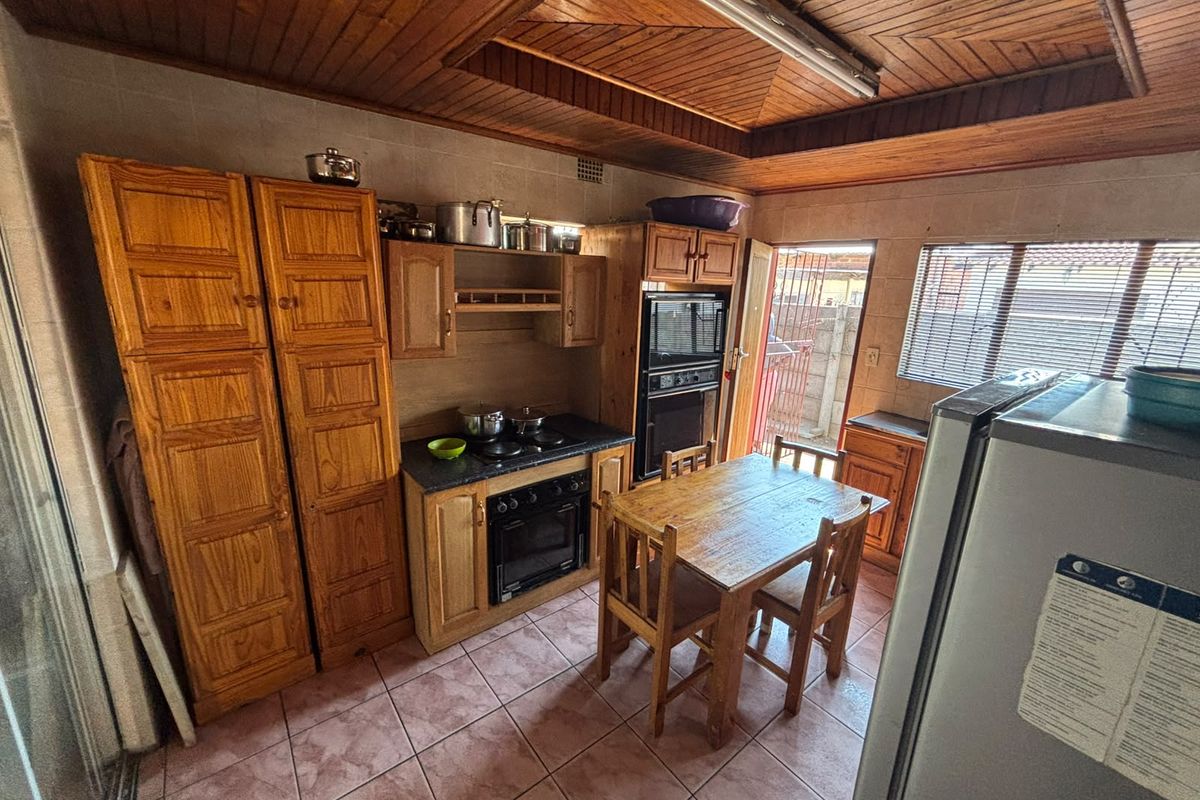 A functional kitchen featuring wooden cabinetry, built-in oven, electric hob, tiled flooring, and a distinctive wooden ceiling with integrated lighting.