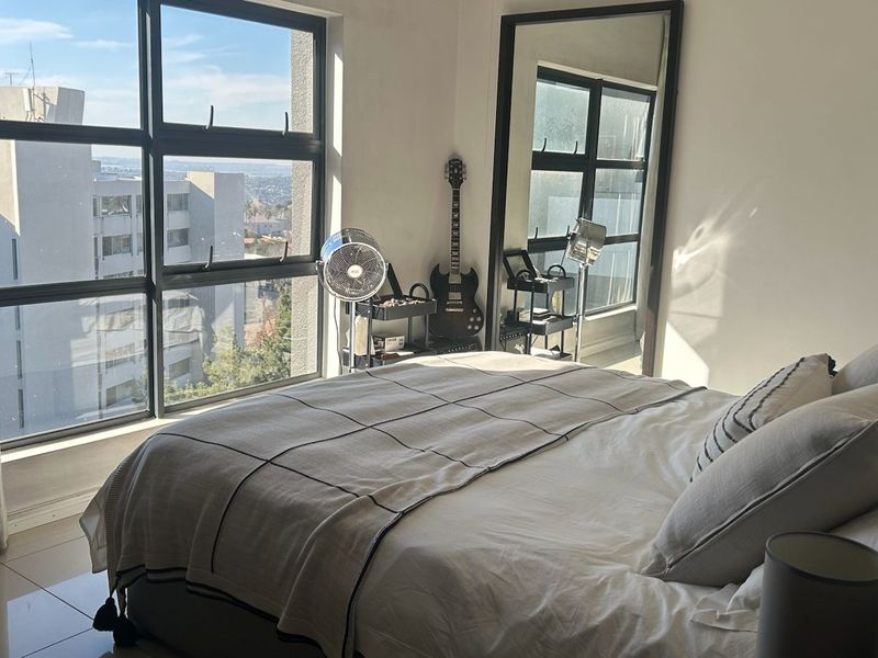 Bright and modern bedroom featuring large windows with city views and sleek tiled flooring.