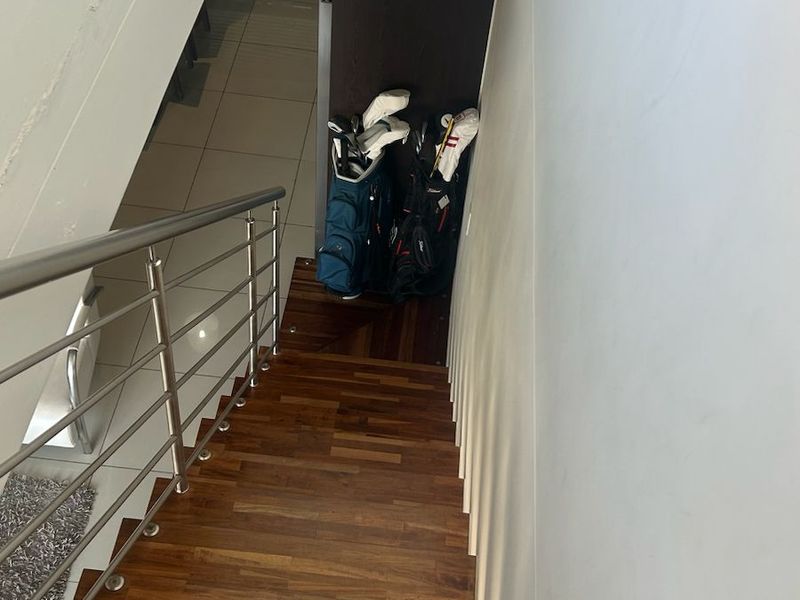 A staircase featuring timber treads and a modern stainless steel balustrade, leading down to a tiled lower level area.