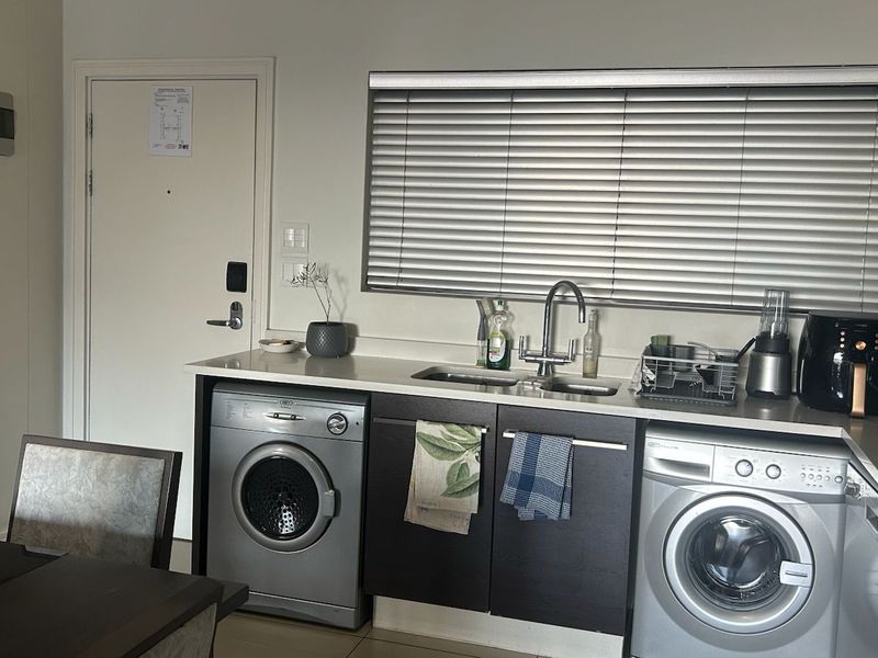 A functional kitchen area featuring integrated cabinetry, stone countertops, a stainless steel sink, and built-in laundry appliance connections.