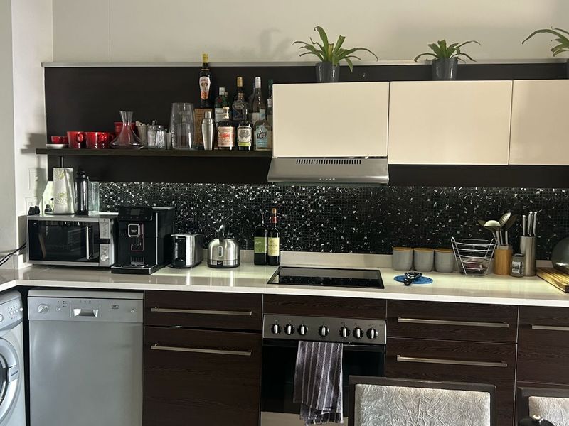 Modern kitchen featuring dark wood cabinetry, stone countertops, a mosaic tile splashback, and integrated appliances including a washing machine and dishwasher.