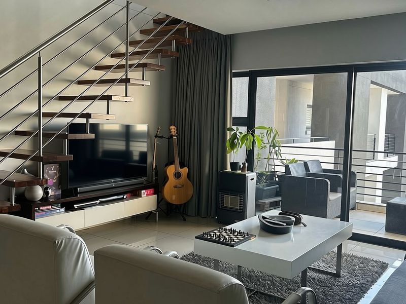 Modern living room featuring a floating staircase with stainless steel balustrades and large sliding glass doors leading to a private balcony.