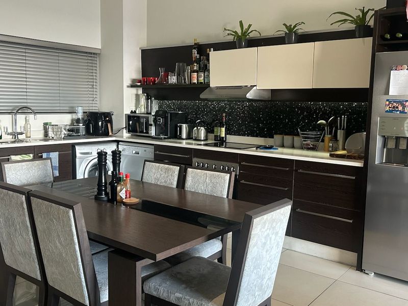Modern open-plan kitchen featuring dark wood cabinetry, integrated appliances, tiled flooring, and a functional layout with an adjacent dining area.