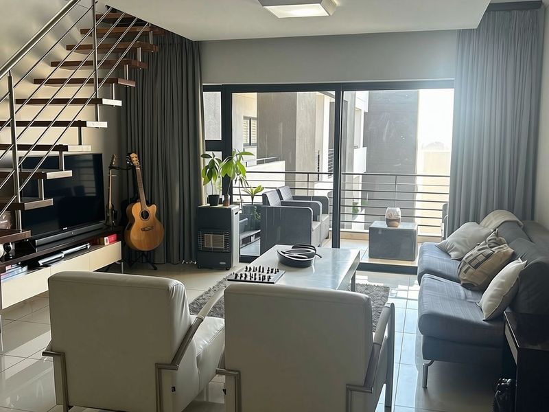 Modern living room featuring a striking floating staircase with stainless steel railings, large sliding doors leading to a balcony, and polished tiled flooring.
