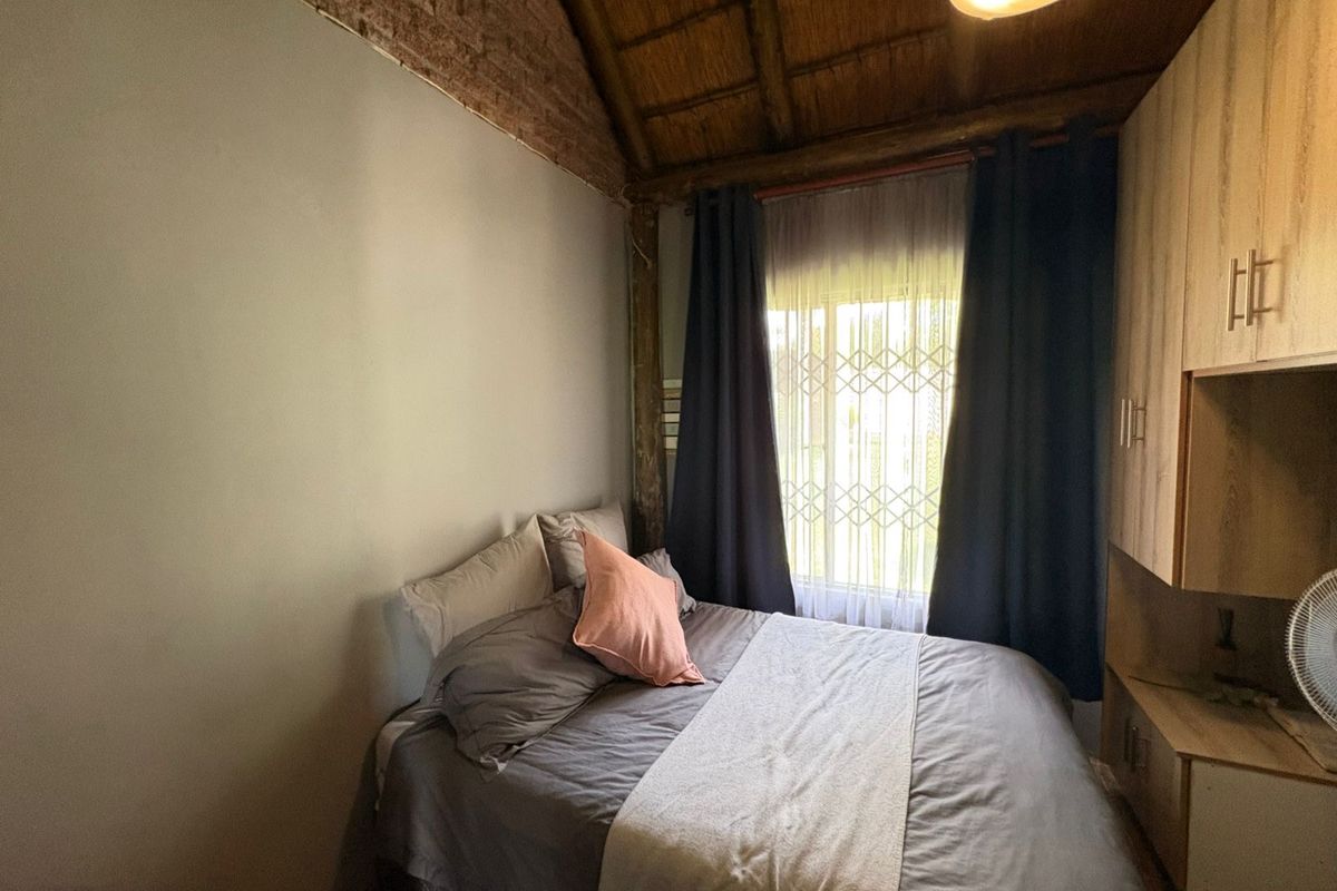 A cozy bedroom featuring a unique exposed brick wall, a traditional thatched roof ceiling, and practical built-in wardrobe storage.