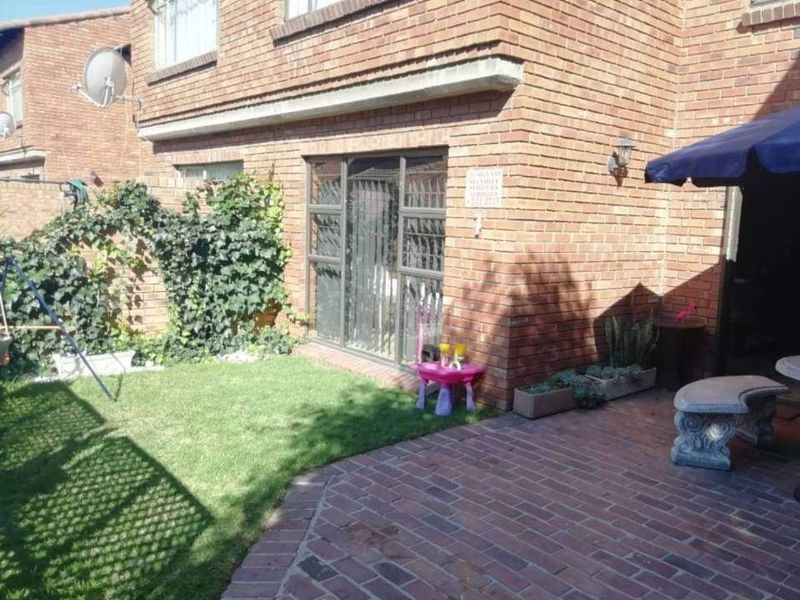 Rear exterior view of the townhouse featuring a brick facade, a paved patio area, and a small private garden with a sliding door entrance.