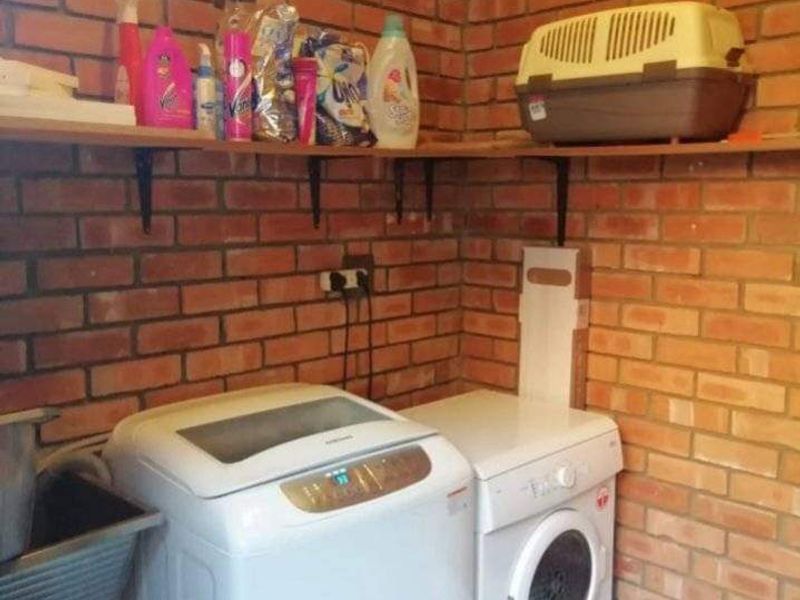 A functional laundry area featuring exposed brick walls, wall-mounted shelving, and space for laundry appliances with a utility sink.