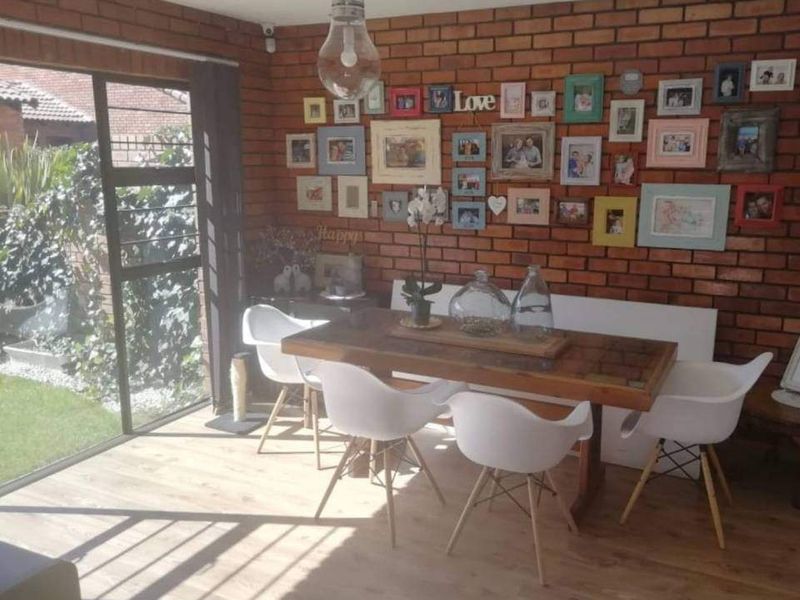 Dining area featuring an exposed brick feature wall, wood-look laminate flooring, and large sliding glass doors providing natural light and garden access.