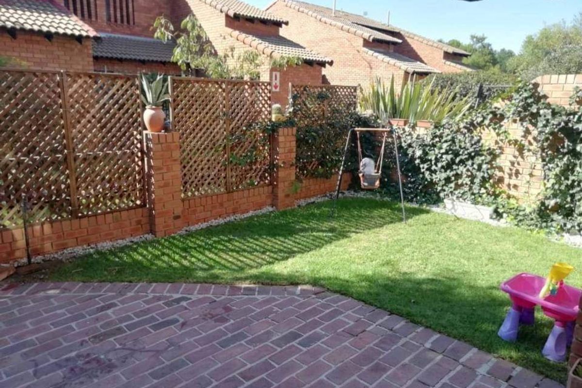 A private rear garden featuring brick paving, a well-maintained lawn, and brick boundary walls with decorative wooden lattice screening.