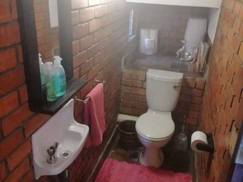 Compact bathroom featuring exposed brick walls, a wall-mounted basin, and a standard toilet, offering a rustic aesthetic with potential for modernization.
