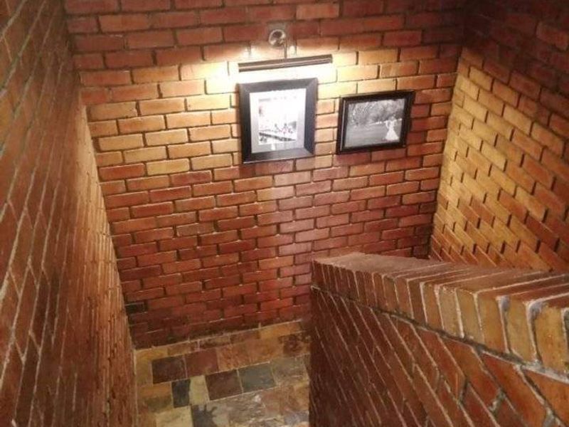 A staircase hallway featuring exposed brick walls and natural stone tile flooring, illuminated by a wall-mounted light fixture.