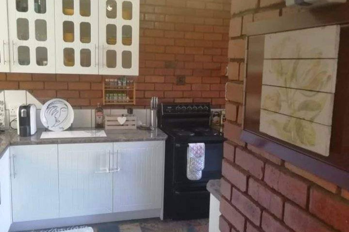 A rustic kitchen featuring exposed brick walls, white cabinetry, slate tile flooring, and a freestanding stove, offering a warm and traditional aesthetic.