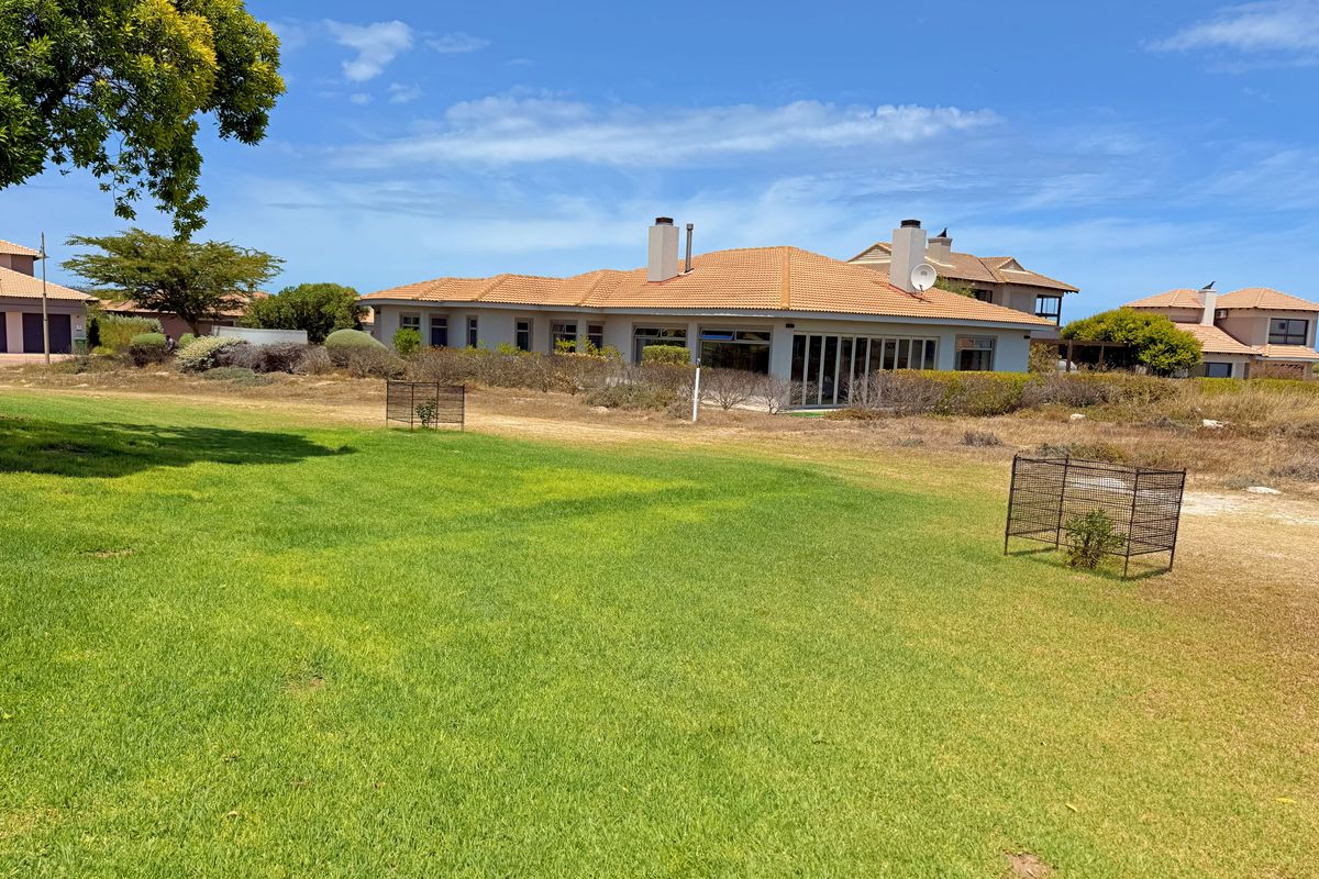 A view of the rear elevation of a single-story house featuring a terracotta tile roof, chimneys, and large sliding glass doors opening to a lawn.