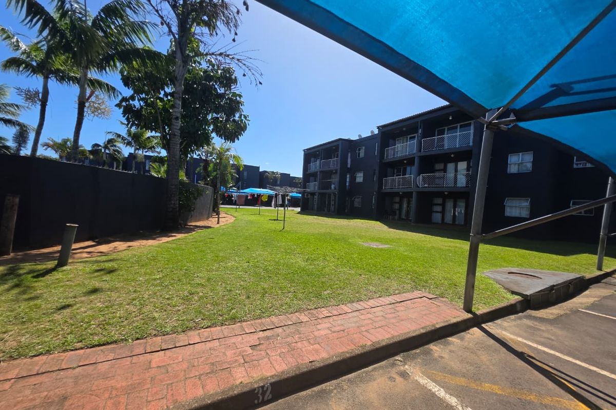 A view of the apartment complex rear garden area featuring a lawn, brick pathways, and balconies overlooking the communal outdoor space.