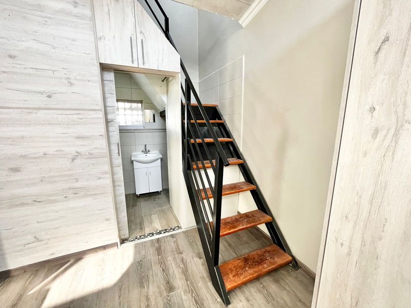 A hallway area featuring built-in cabinetry, a staircase with a metal handrail, and access to a small bathroom with a vanity basin.