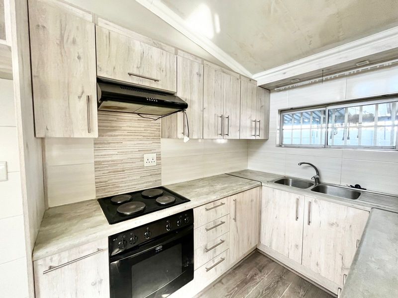 Functional kitchen featuring light wood-grain cabinetry, laminate countertops, built-in electric oven and hob, and a double stainless steel sink with tiled splashback.
