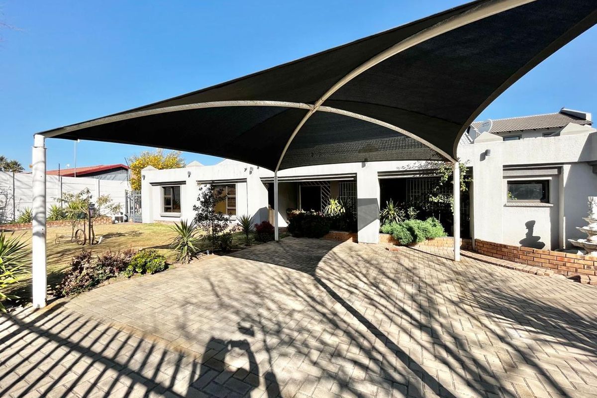Rear exterior view of the townhouse featuring a paved patio area covered by a large shade sail and a small garden space.
