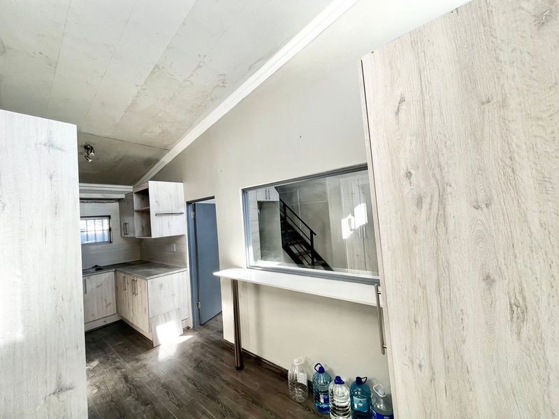 A compact kitchen area featuring light wood-look cabinetry, a breakfast bar, and an internal window, requiring ceiling repairs and cosmetic updates.