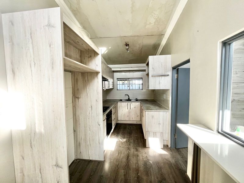 A compact kitchen featuring light wood-look cabinetry, laminate countertops, and integrated appliances, currently requiring ceiling completion and final finishing touches.