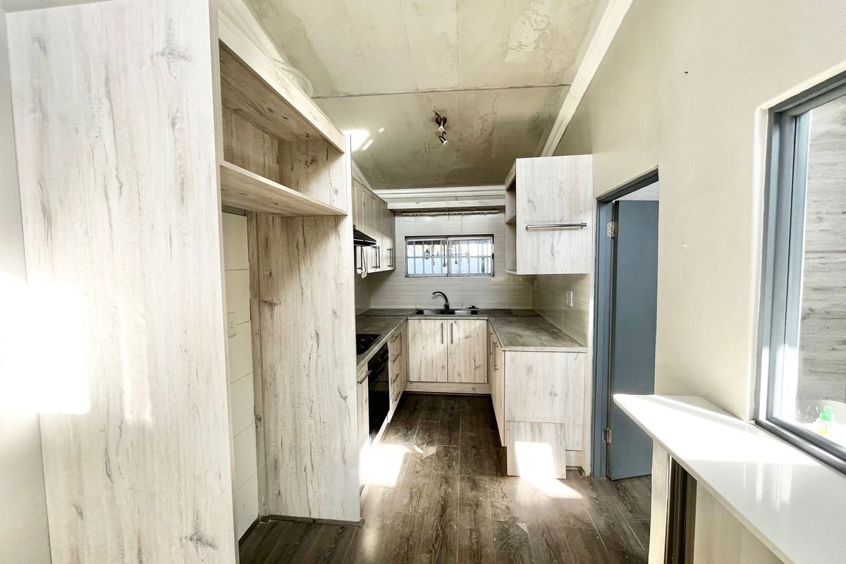 A compact kitchen featuring light wood-look cabinetry, laminate countertops, and integrated appliances, currently requiring ceiling completion and final finishing touches.