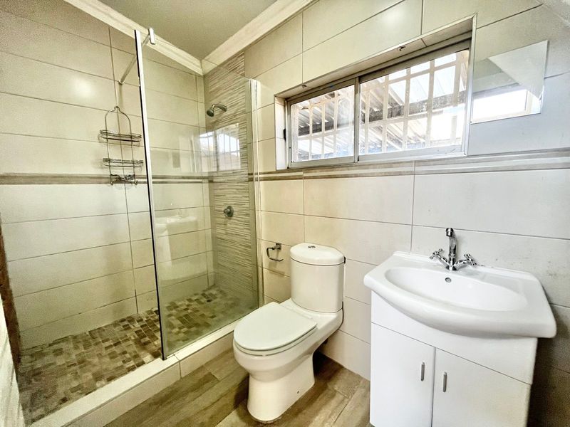 A clean, modern bathroom featuring a glass-enclosed shower, a white vanity with a basin, and neutral wall and floor tiling.