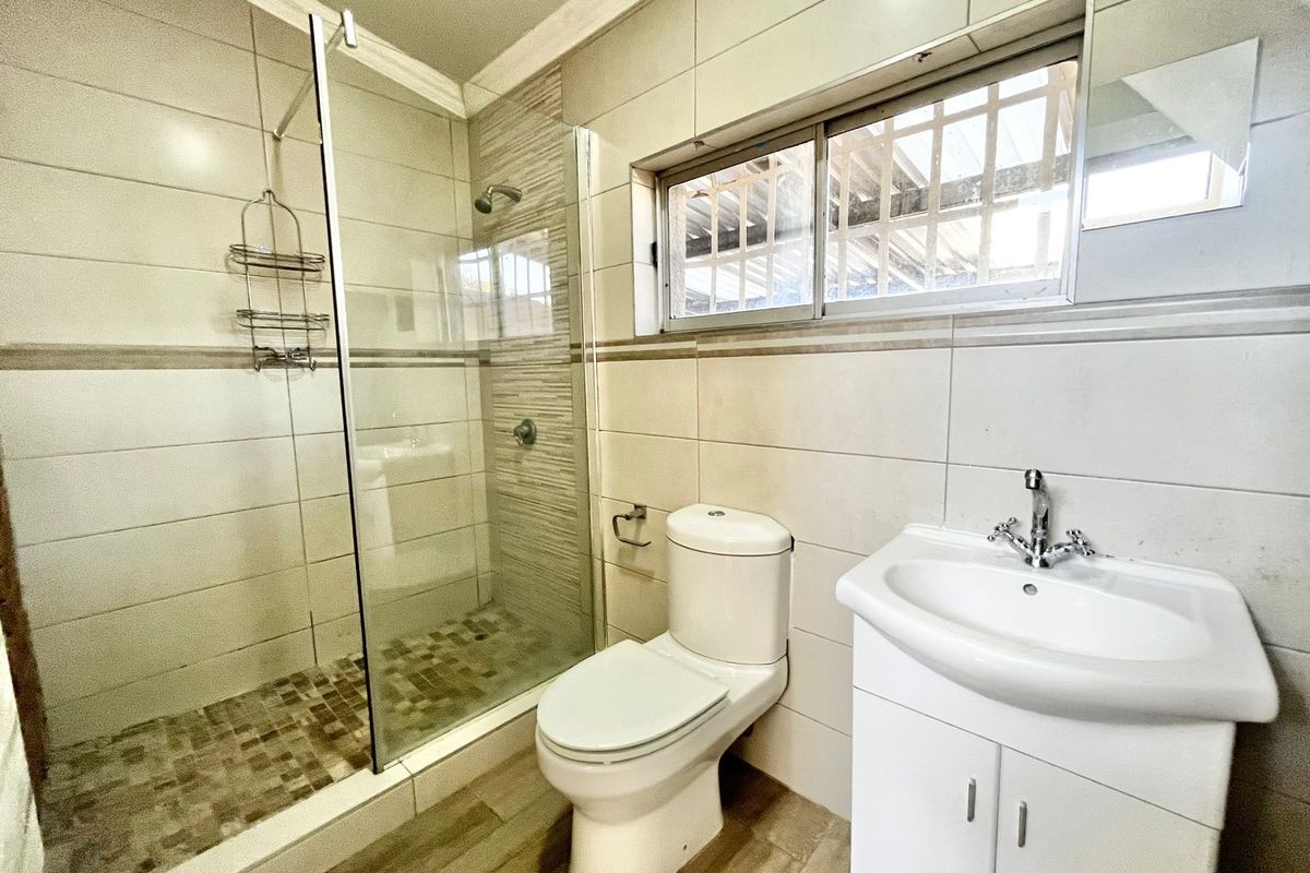 A clean, modern bathroom featuring a glass-enclosed shower, a white vanity with a basin, and neutral wall and floor tiling.